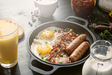 English breakfast on a dark table. fried eggs with bacon canned beans and sausage. near coffee, orange juice and pancakes with butter and honey