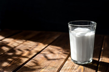 glass of milk on a wooden table. dark background, bright contrasting sun