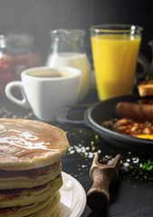English breakfast on a dark table. fried eggs with bacon canned beans and sausage. near coffee, orange juice and pancakes with butter and honey