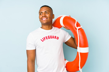 Young latin life guard isolated on blue background looks aside smiling, cheerful and pleasant.