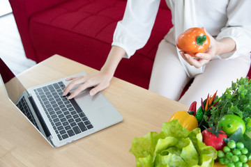 Close up, Nutritionists hold orange bell peppers and find information about their properties and nutritional values ​​via laptop.  She is doing research and education about herbs. Healthcare concept.
