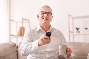 Elderly man watching tv with tea sitting on sofa