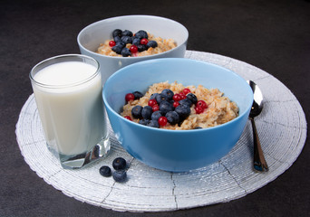 Oatmeal porridge with fresh blueberries, in blue bowl and glass milk. Healthy breakfast, healthy eating, vegan food concept. Colorful breakfast for kids, selective focus, close up