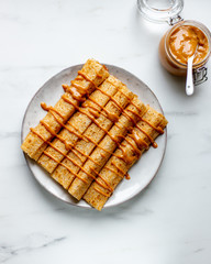 french crepe filled with caramel fudge and decorated with chocolate fudge, berries castor sugar and mint leaves on marble background with copy space