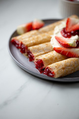 french crepe filled with caramel fudge and decorated with chocolate fudge, berries castor sugar and mint leaves on marble background with copy space
