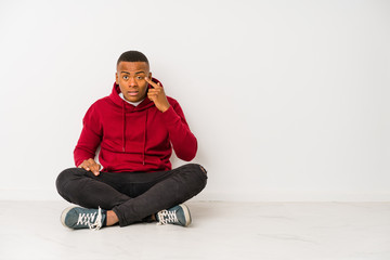 Young latin man sitting on the floor isolated showing a disappointment gesture with forefinger.