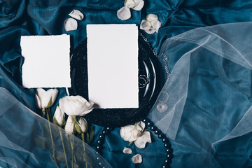 Wedding invitation mockup with old black plate, roses, papers on silk blue background. Top view, flat lay. Wedding stationary. Perfect for presentation of your invitation, menu, greeting cards