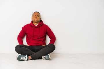 Young latin man sitting on the floor isolated blows cheeks, has tired expression. Facial expression concept.