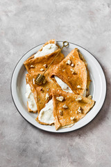 Crepes or thin pancakes with cottage cheese cream, honey and walnut. Traditional Maslenitsa (Shrovetide) meal and tasty breakfast on gray background. Copy space, top view.