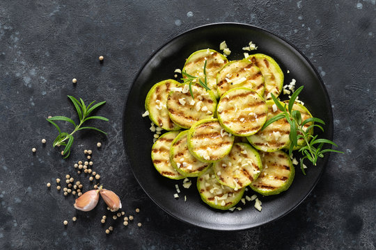 Grilled zucchini, courgette with garlic and rosemary on plate, top view