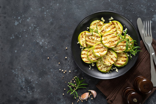 Grilled zucchini, courgette with garlic and rosemary on plate, top view