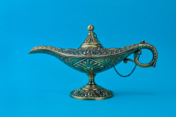 Antique golden colored oil lamp with rust displayed over a blue background