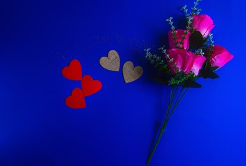 two wooden and three red hearts lie with artificial pink flowers on a blue background
