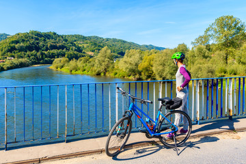 Young woman tourist looking at Dunajec river from bridge on Velo Dunajec cycling road near Nowy...