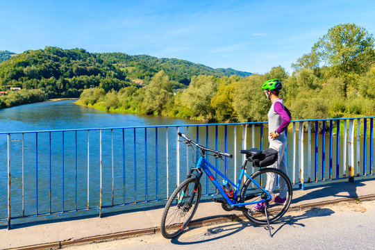 Young woman tourist looking at Dunajec river from bridge on Velo Dunajec cycling road near Nowy Sacz, Poland