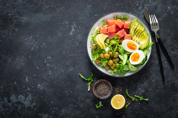 Ketogenic, paleo diet lunch bowl with salted salmon fish, lemon, avocado, olives, boiled egg, cucumber, green lettuce salad and chia seeds, healthy food trend, top view