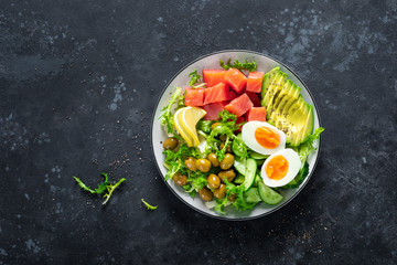 Fototapeta na wymiar Ketogenic, paleo diet lunch bowl with salted salmon fish, lemon, avocado, olives, boiled egg, cucumber, green lettuce salad and chia seeds, healthy food trend, top view