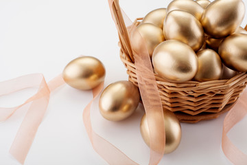 Golden eggs in a wicker basket, on a white background, with space for text, with copy space. Concept backgrounds for Easter, abundance and symbols of wealth.