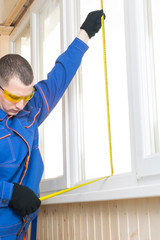 a worker in a blue uniform measures a plastic window on the balcony with a meter