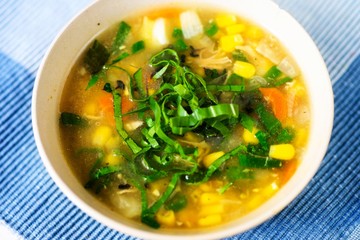 Corn soup with sliced green onion in white plate on blue.