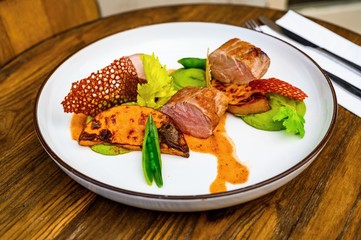 Pork tenderloin,pea puree an pods, pumpkin and beet chips in arrangemnt on white plate.