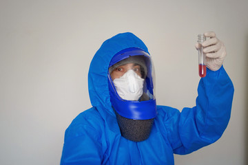 Fototapeta na wymiar A man in a blue protective suit holds a test tube in his hands. The concept of open vaccines against coronavirus