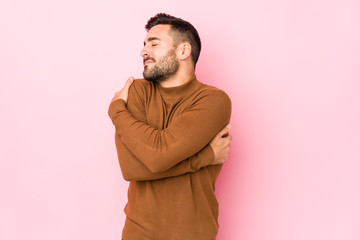 Young caucasian man against a pink background isolated hugs, smiling carefree and happy.