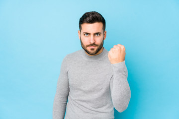 Young caucasian man against a blue background isolated showing fist to camera, aggressive facial expression.