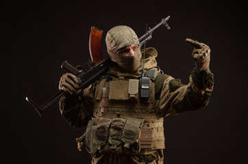 a saboteur soldier in military clothing with a weapon on a dark background shows gestures