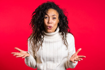 Pretty female shocked model on red background. OMG, wow effect. African girl with long hair with delight. Surprised excited happy woman in sweater