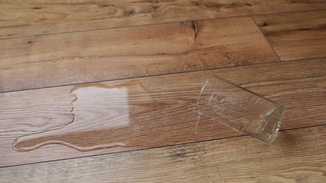 Hand picking up a glass of water that has fallen to the laminate floor of wood