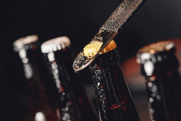 Glass ice cold bottles of beer with opener cap on dark background