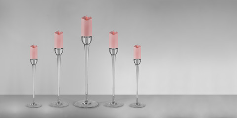 Modern style glass pastel coloured candlesticks with pink candles and flames on the floor. Home decoration. Interior objects with clean and isolated grey background.