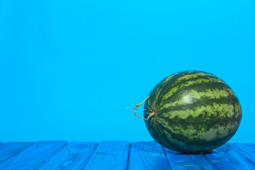 One watermelon on a wooden table with a blue background. Summer concept