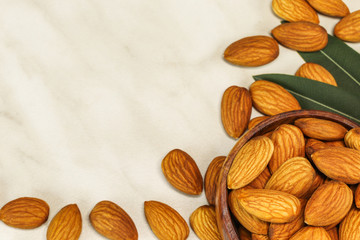 Almond nuts lie in a brown wooden bowl and on white marble