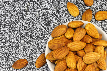 Almond nuts lie in a white glass bowl and on gray-white marble