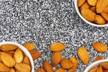 Almond nuts lie in three white glass bowls and on gray-white marble