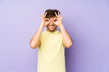 Young arabian man isolated on a purple background showing okay sign over eyes