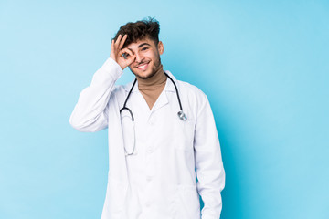 Young arab doctor man idolated excited keeping ok gesture on eye.