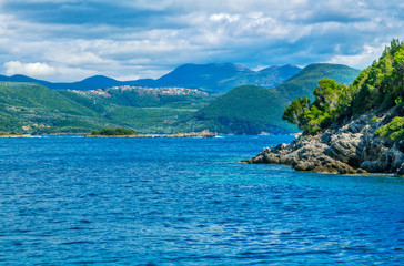 Obraz premium Beautiful summer landscape with sea lagoon, rocks and cliffs, green trees on the coast, mountains on the horizon and clouds on the sky. 