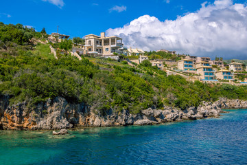 New villas and houses on the cliff over the sea with rocks in turquoise water. Summer landscape- green trees and blue sky. 