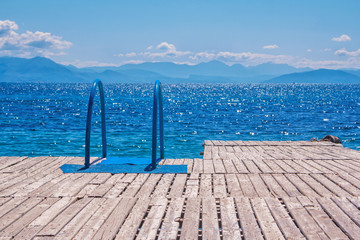 View of wooden pier with blue bathing ladder. Summer landscape with turquoise calm sea water,...