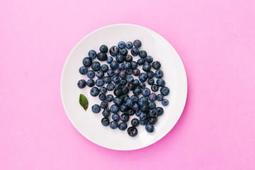 Fresh blueberries in a white plate on a pink background. Top view, flat lay.