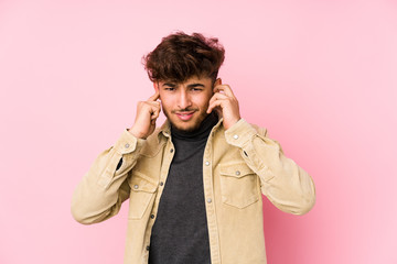 Young arabian man posing in a background isolated covering ears with hands.