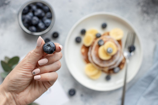 blueberries in a female hand with a beautiful nude manicure, over a table with pancakes. horizontal image, top view