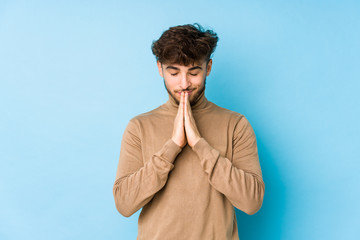 Young arabian man isolated holding hands in pray near mouth, feels confident.