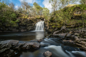 Dreamy waterfall and river in sunny hilly woodland