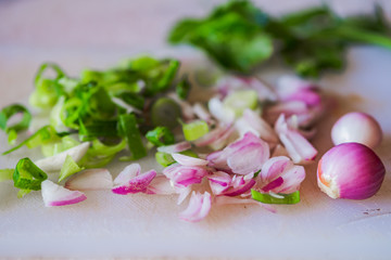 Shredded onnions, scallions, and celery leaves on white surface.