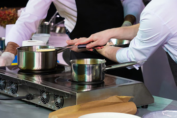 Joint work of two chefs. Professional cooking. Restaurant. Cafe. Metal ladles on the stove. The preparation of sauces. Food industry. The manufacturer of the cream.