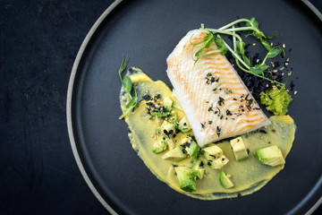 Gourmet Kabeljau Fisch Filet gebraten mit Kaviar, Avocado Scheiben und Mango Senf Creme als Draufsicht auf einem Modern Design Teller mit Textfreiraum links